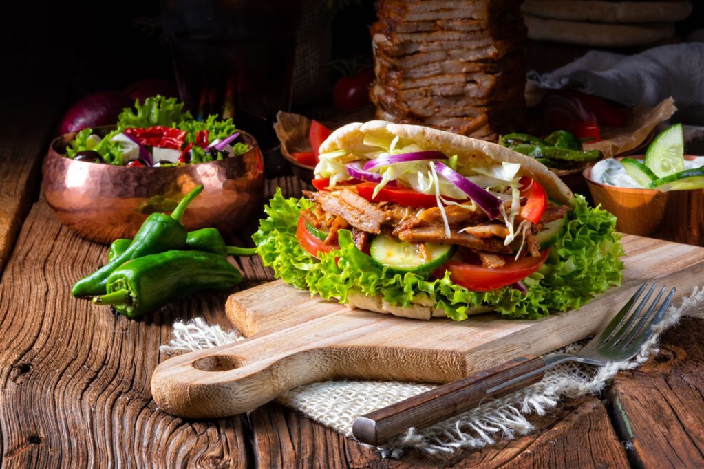 Ein rustikaler Tisch mit einem belegten Sandwich und frischem Gemüse.