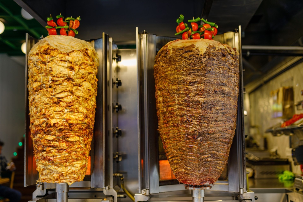Zwei große, gebratene Fleischspieße auf Rotisserie-Geräten in einer Profiküche.
